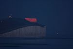 C03 : La super-Lune se lève derrière les nuages et les falaises calcaires de la Manche portant le phare de Belle Tout (côté britannique). Le point lumineux à droite est un ferry ou un cargo. Le 27 avril 2021 depuis Cuckmere Haven, dans l'Est du  Sussex. EOS 40D, 400mm, f/5.6, 800 ISO, 2,5s.